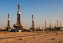 Shura Council Approves Bahrain Gas Exploration Concession Oil drilling site in a desert with multiple derricks, tanks, and equipment under a clear sky at sunset.