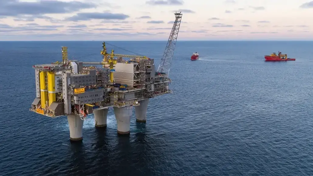 Offshore oil platform on three legs in the sea with a crane, ships visible in the distance.