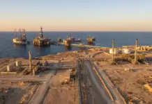 Egypt Discusses WDDM Area Investment with Oil Companies Aerial view of an offshore oil field with multiple platforms connected by pipelines along a desert coastline at sunset.