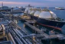 LNG Supply Deal Expands INEOS Energy Asian Market Presence LNG carrier docked at an offshore processing facility with large spherical storage tanks and complex piping at twilight.