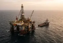 Egypt Eyes Further UAE Investment in Oil and Gas Sector Offshore oil rig with cranes and a tugboat nearby at sea during sunset