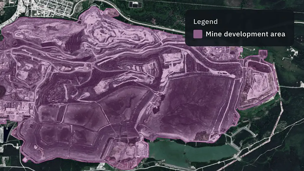Satellite map showing a large pink-highlighted mine development area with contour-like terracing and surrounding roads. The legend reads 'Mine development area'.