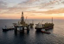 SLB, Vår Energi Advance Well and Integrated Field Planning Offshore oil platform with cranes and supply vessels at sunset, floating on calm sea.