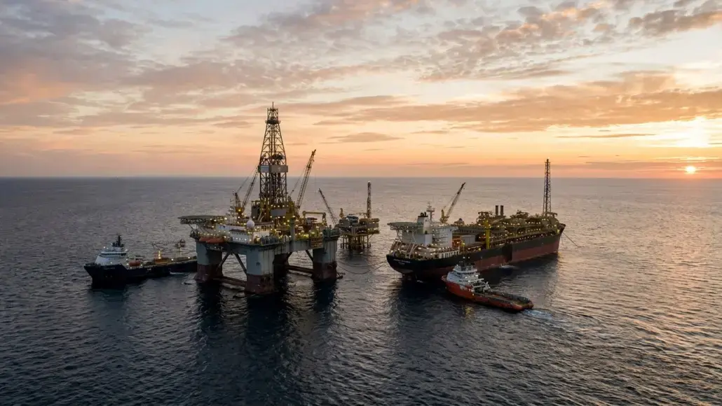 Offshore oil platform with cranes and supply vessels at sunset, floating on calm sea.