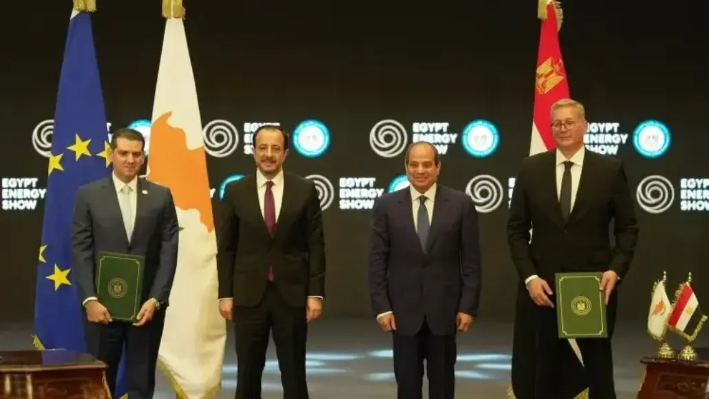 Four men in suits pose on stage with flags (EU and national flags) and green folders at the Egypt Energy Show.