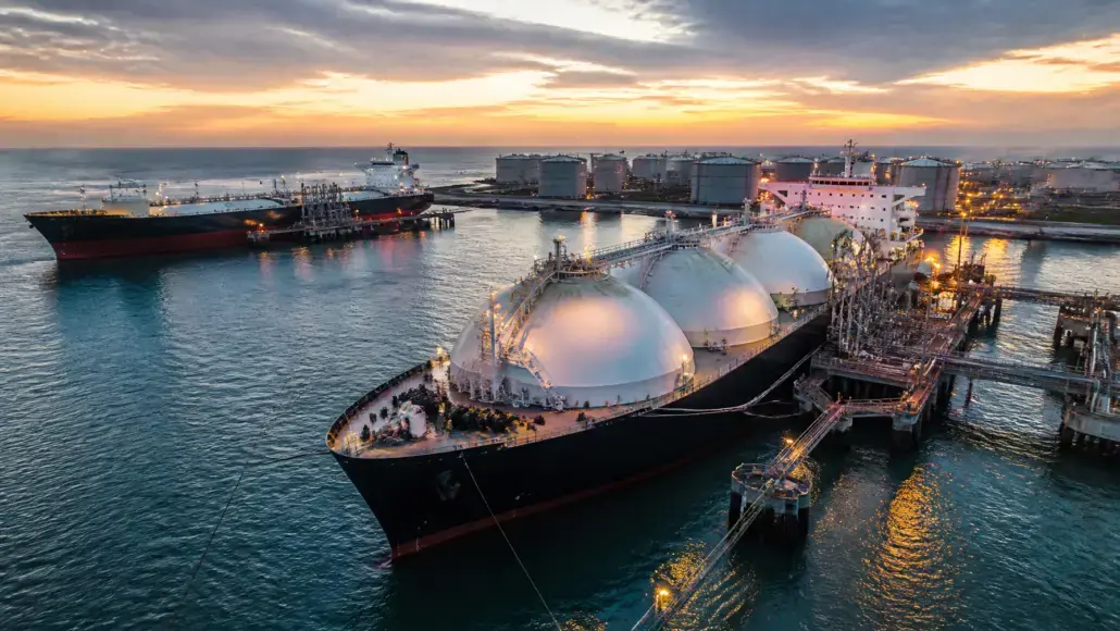 LNG carrier with three white spherical storage tanks docked at an industrial port at sunset